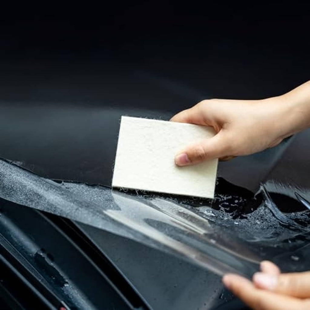 Hand applying a light beige felt squeegee pad to a glossy dark vinyl surface