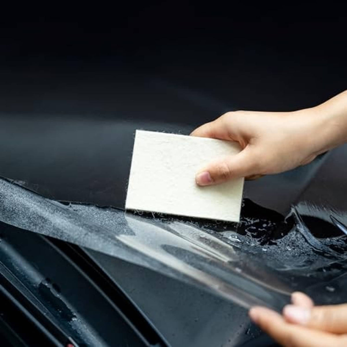 Hand applying a light beige felt squeegee pad to a glossy dark vinyl surface