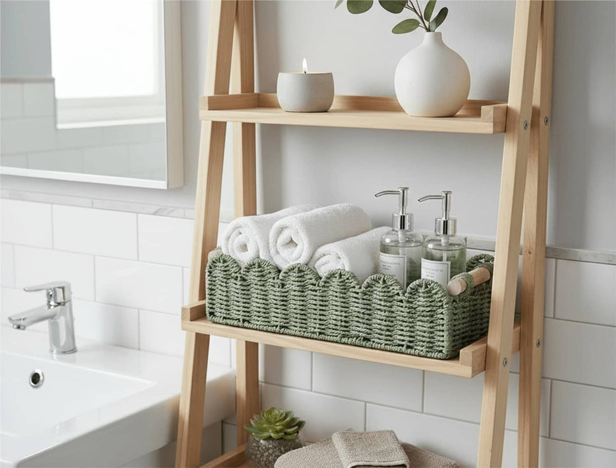 Green woven scalloped basket with wood handles holding folded towels and bottles