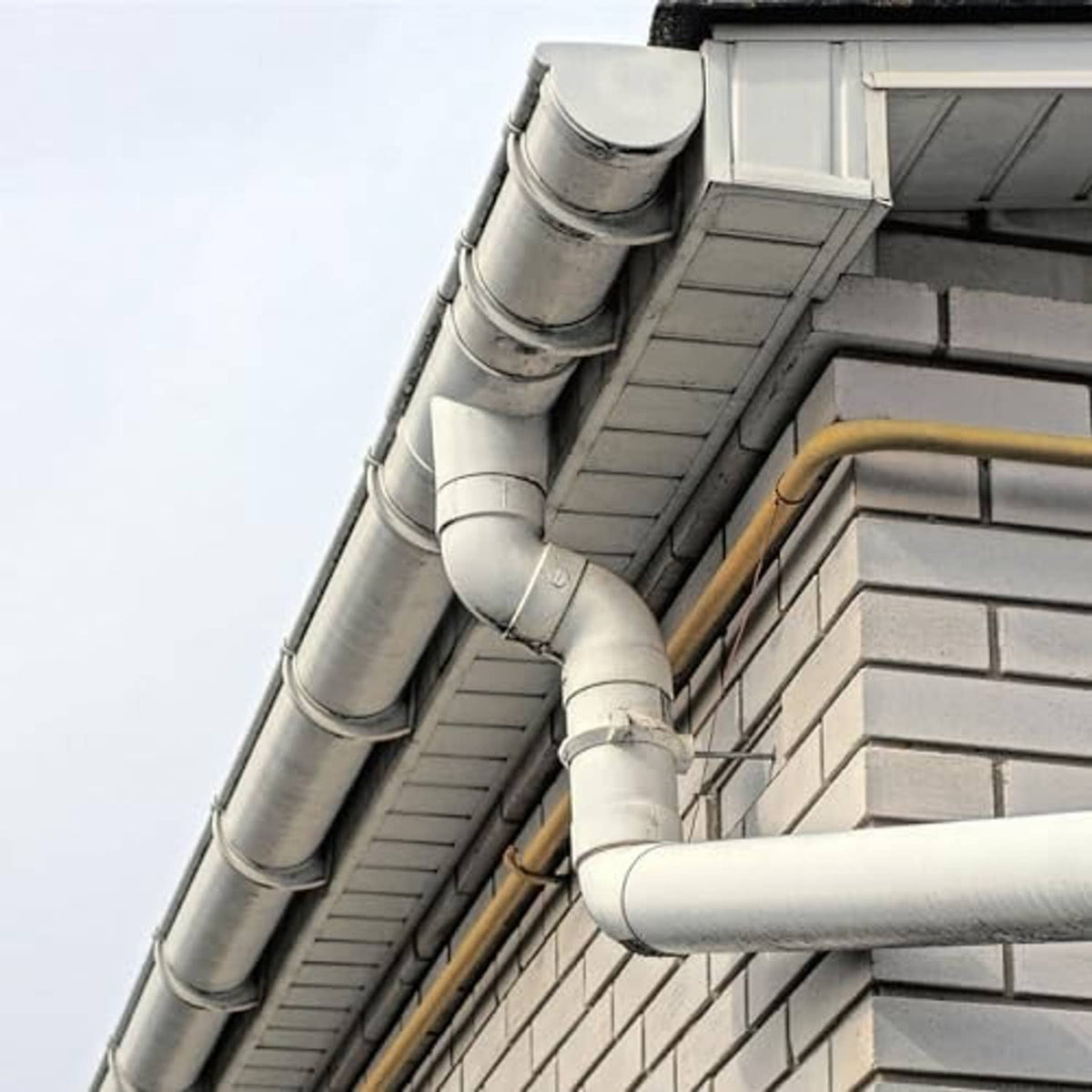 Galvanized split-ring pipe brackets securing conduit pipes on a building eave.