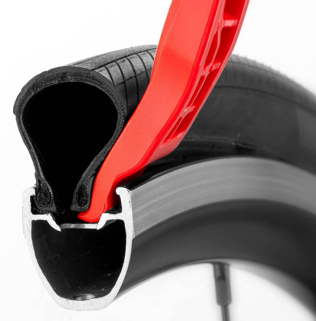 Red bicycle tire lever prying lip positioned on a black tire bead.