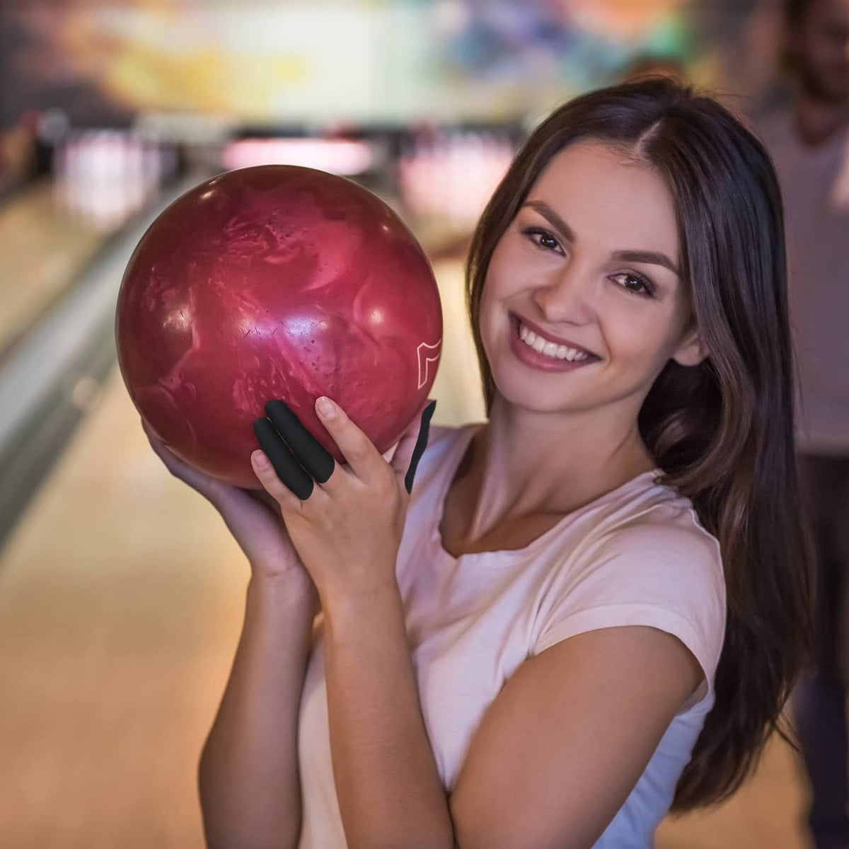 Woman holding a bowling ball with black finger tape on the thumb and finger holes