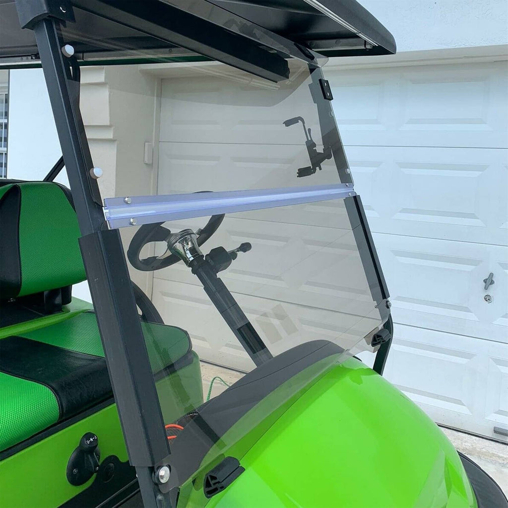 Fold-down tinted golf cart windshield with dark frame, mounted on a green cart