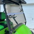 Fold-down tinted golf cart windshield with dark frame, mounted on a green cart