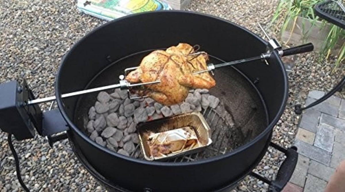 Black rotisserie grill with roasted chicken on a wire spit over coals