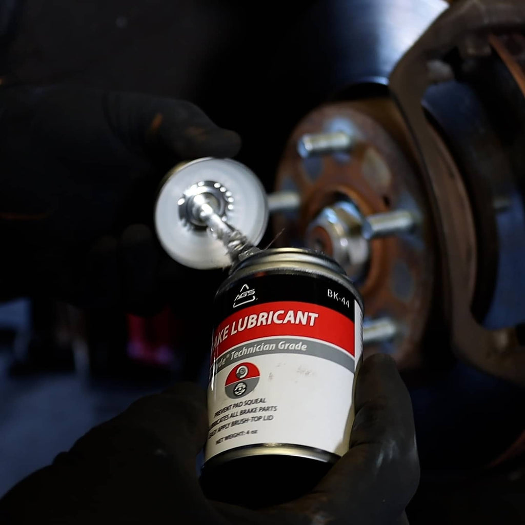 Gloved hand holds AGS SIL-Glyde silicone brake grease near brake caliper