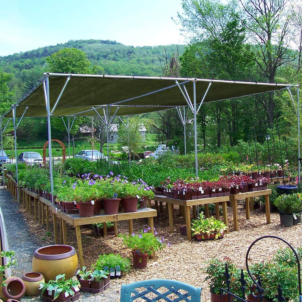 Green waterproof tarp canopy stretched on metal frame over rows of potted plants