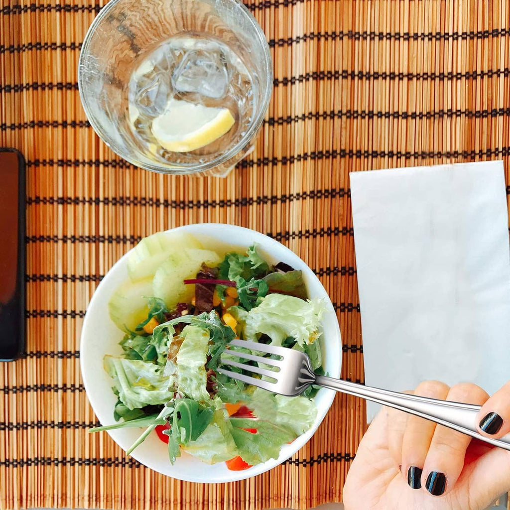 Hand holding a stainless 7-inch salad fork with 3 tines over a leafy salad bowl