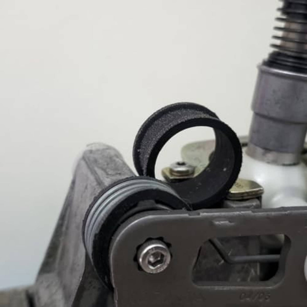 Black rubber shifter reverse lever bushing with adjacent spring near metal lever base.