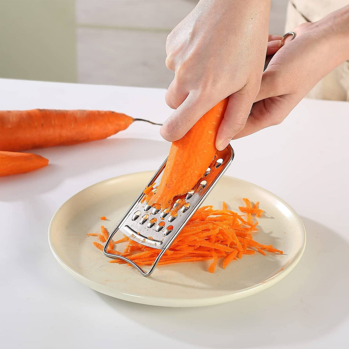 Stainless steel box grater shredding orange carrot on a plate