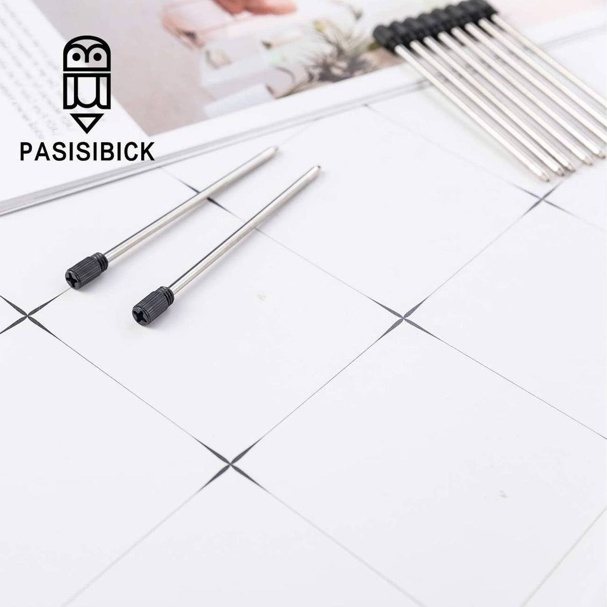 Ballpoint pen refills with black caps on metal shafts, two pens laid on white surface