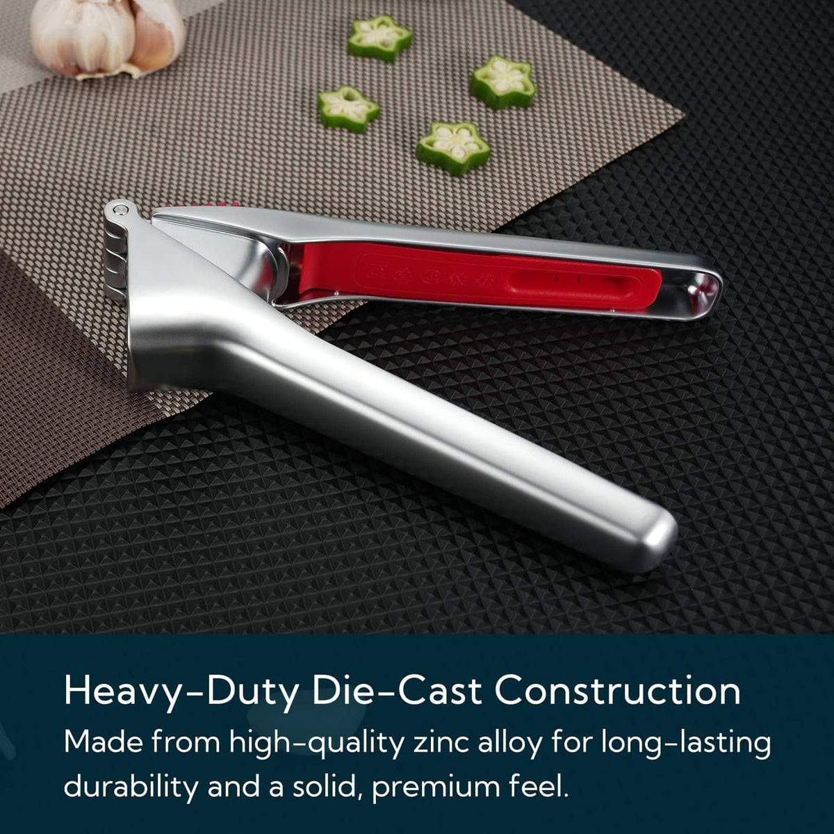 Heavy-duty garlic press with red cleaning scraper bar on textured mat