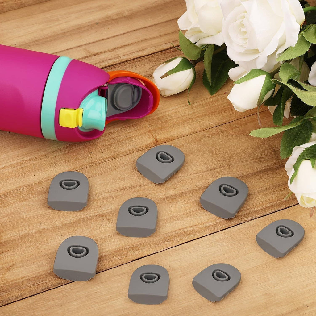 Gray silicone bottle stoppers arranged on wood near an open magenta bottle lid