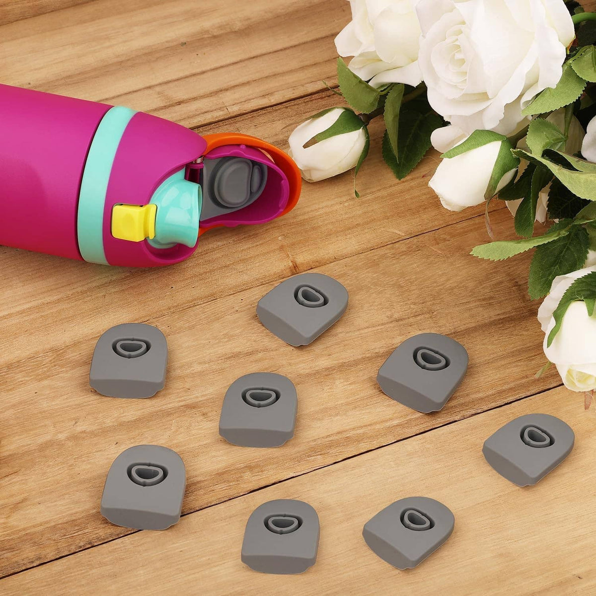 Gray silicone bottle stoppers arranged on wood near an open magenta bottle lid