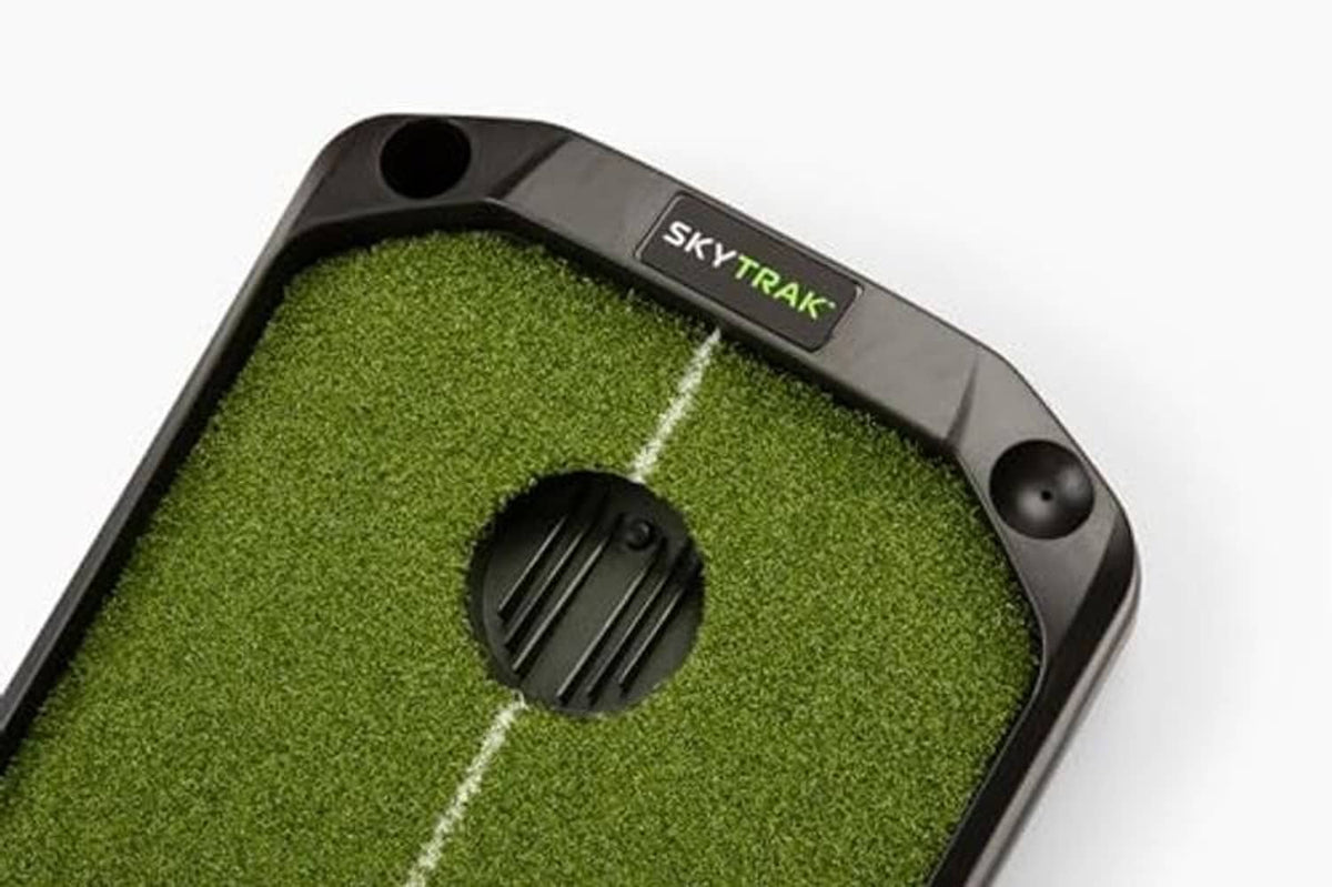 Putting mat with skytrak label and black ball return housing on green turf