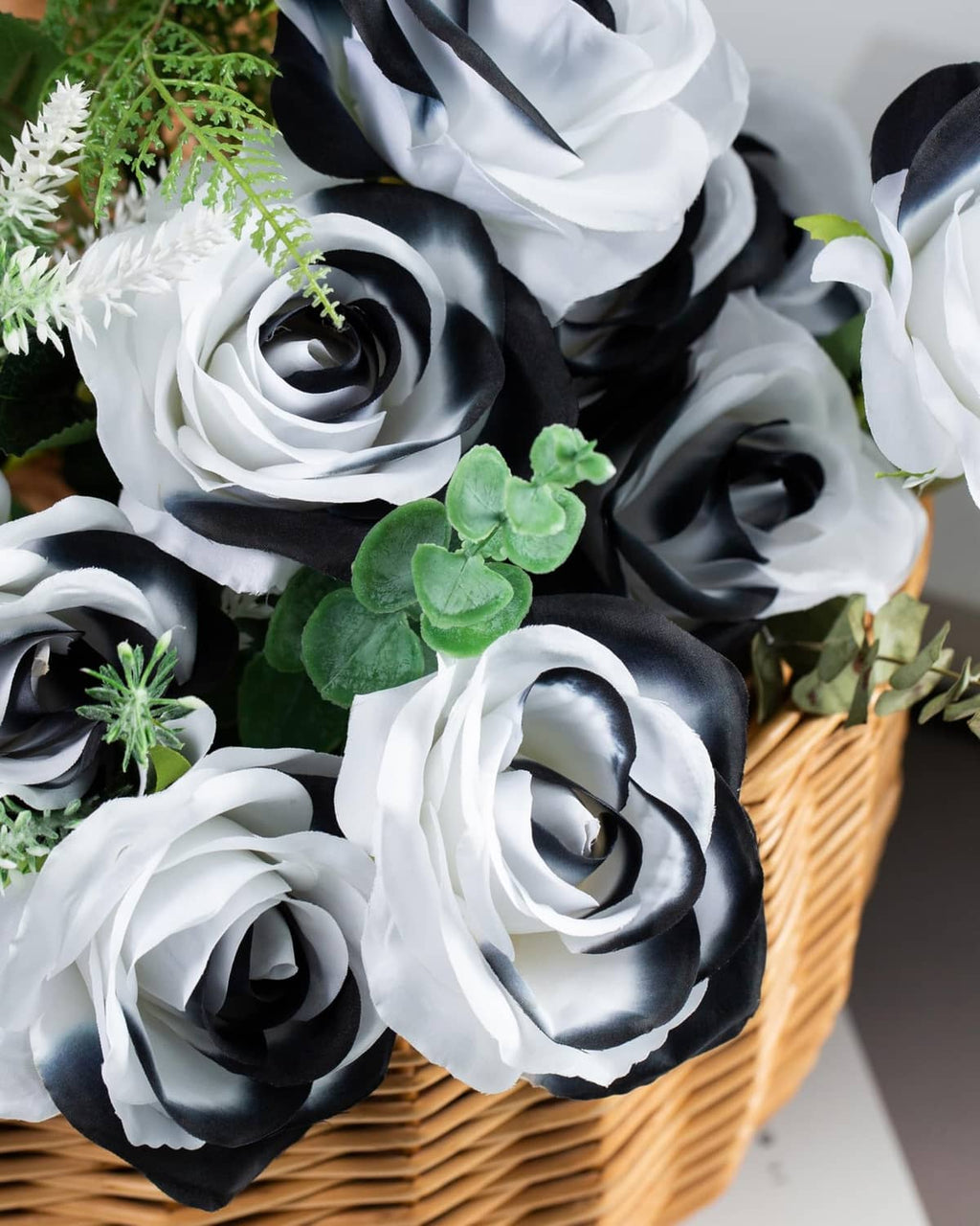 Artificial rose bouquet in wicker basket with white and black blooms and green leaves