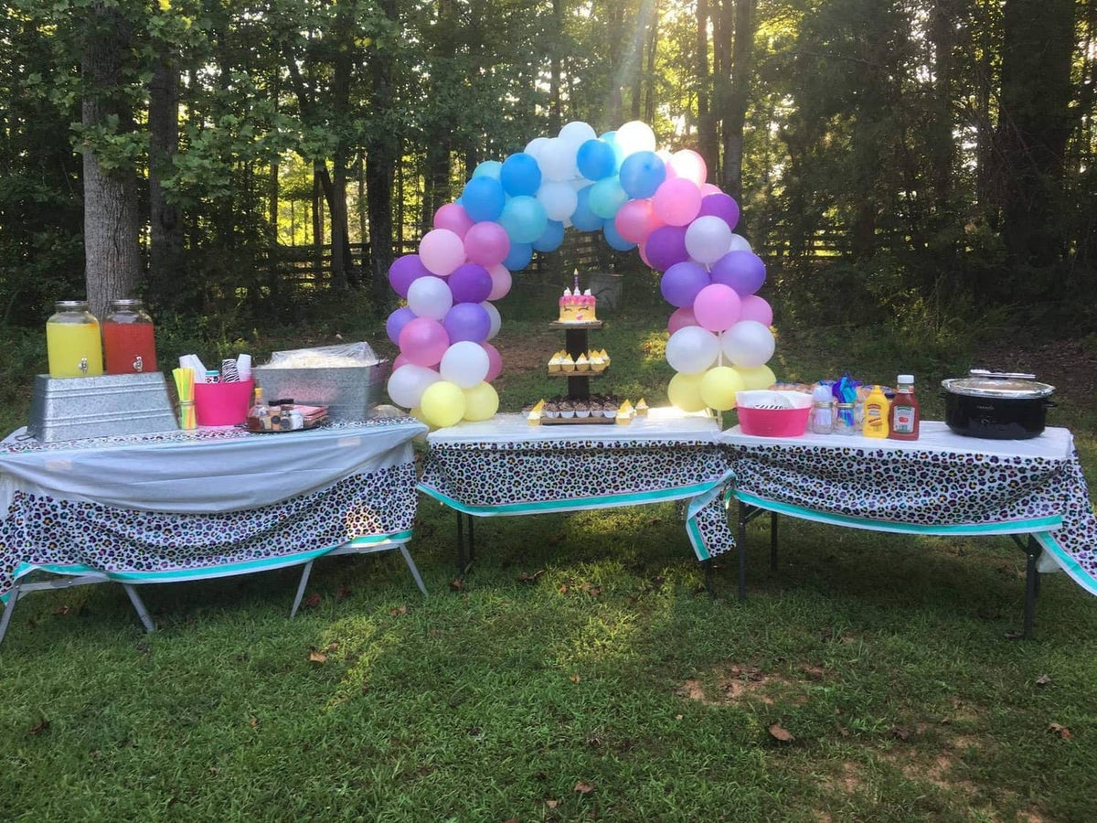 Outdoor table balloon arch with pastel purple, pink, blue, and yellow balloons