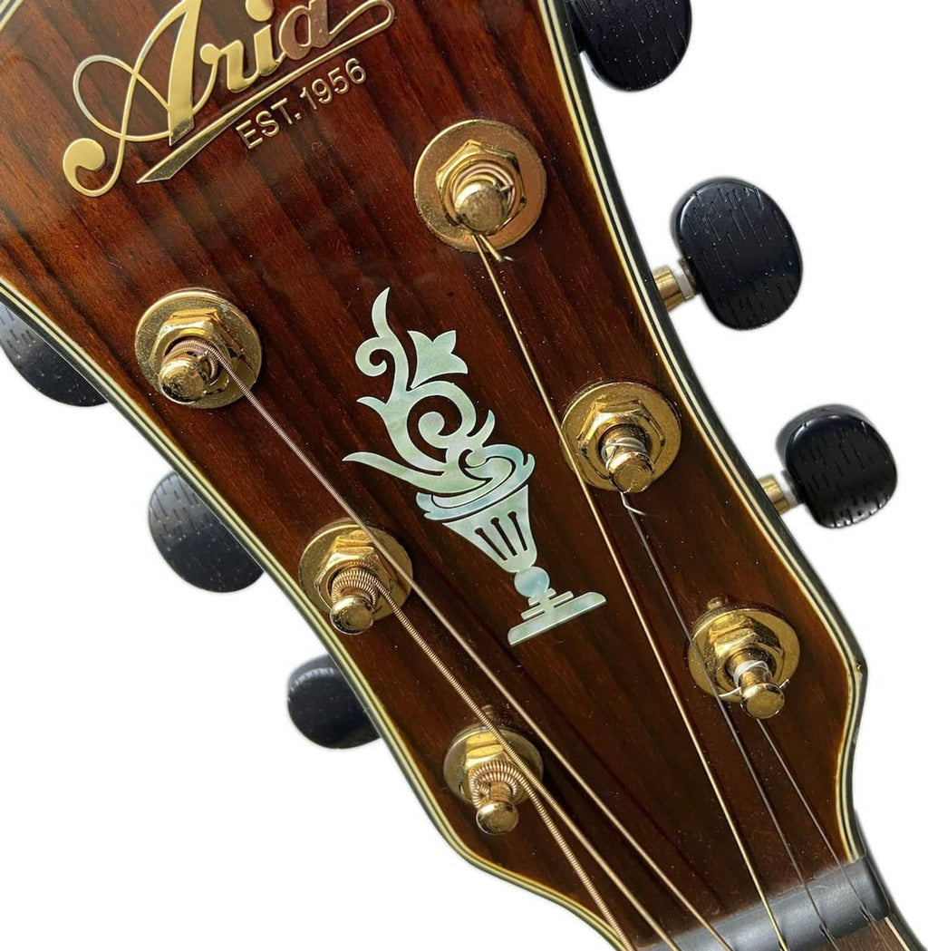 Inlay decal on wooden headstock with teal cup and candlestick icons near gold tuners