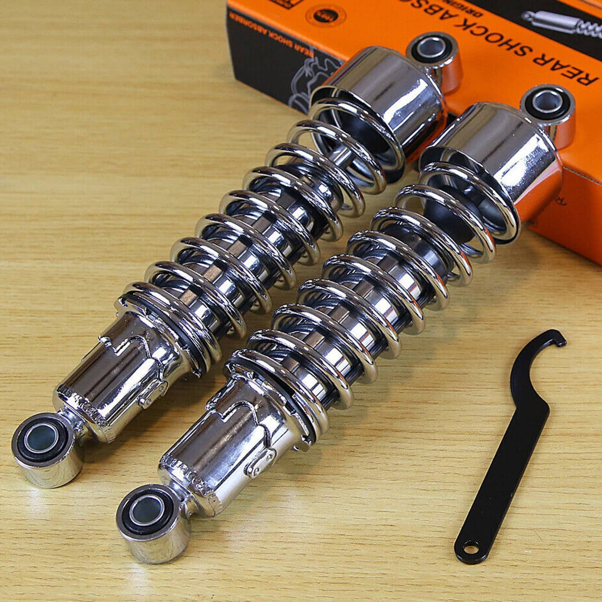 Two chrome rear shocks with black coil springs, eyelet mounts, and black installation tool