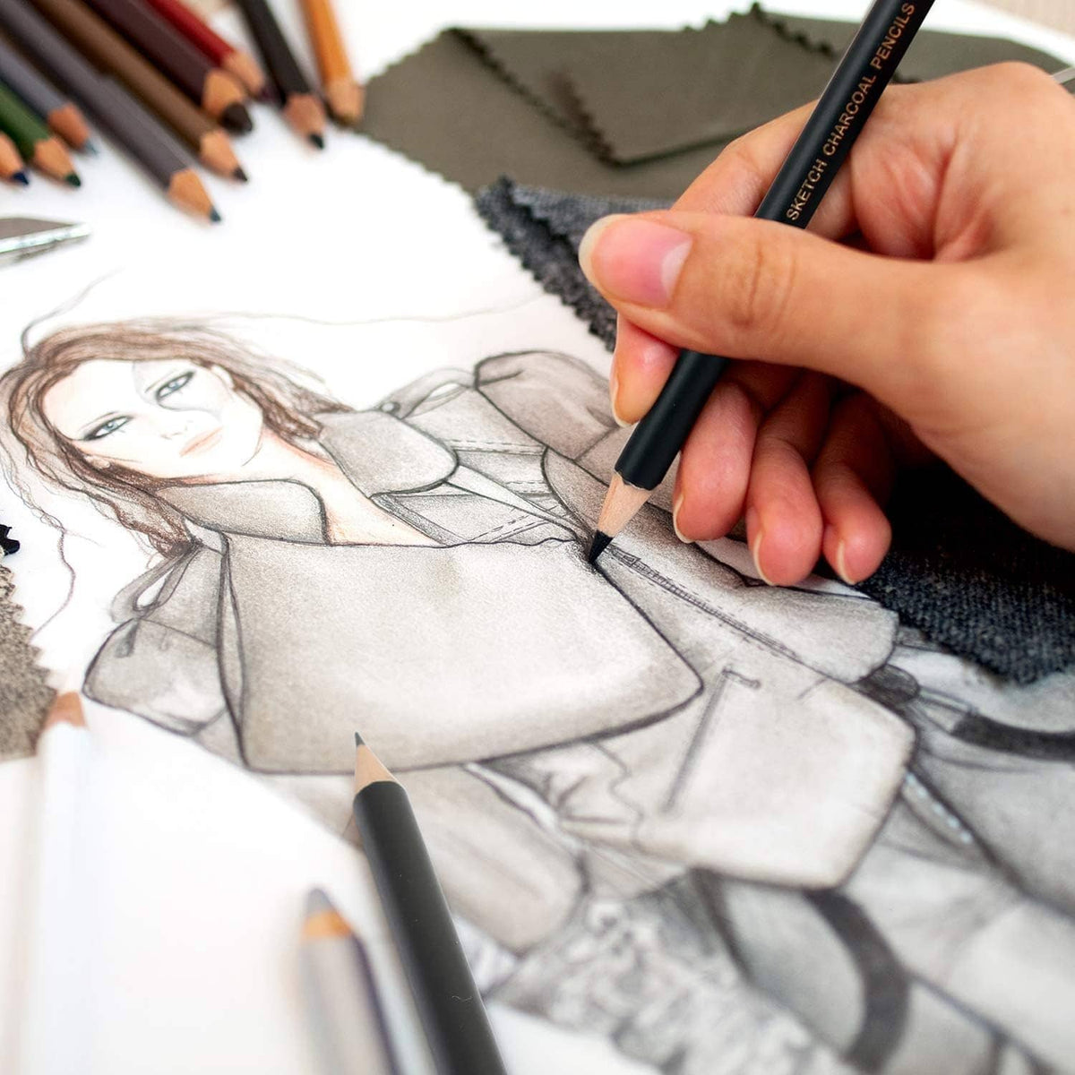 Hand holding a charcoal pencil, shading a portrait sketch on paper