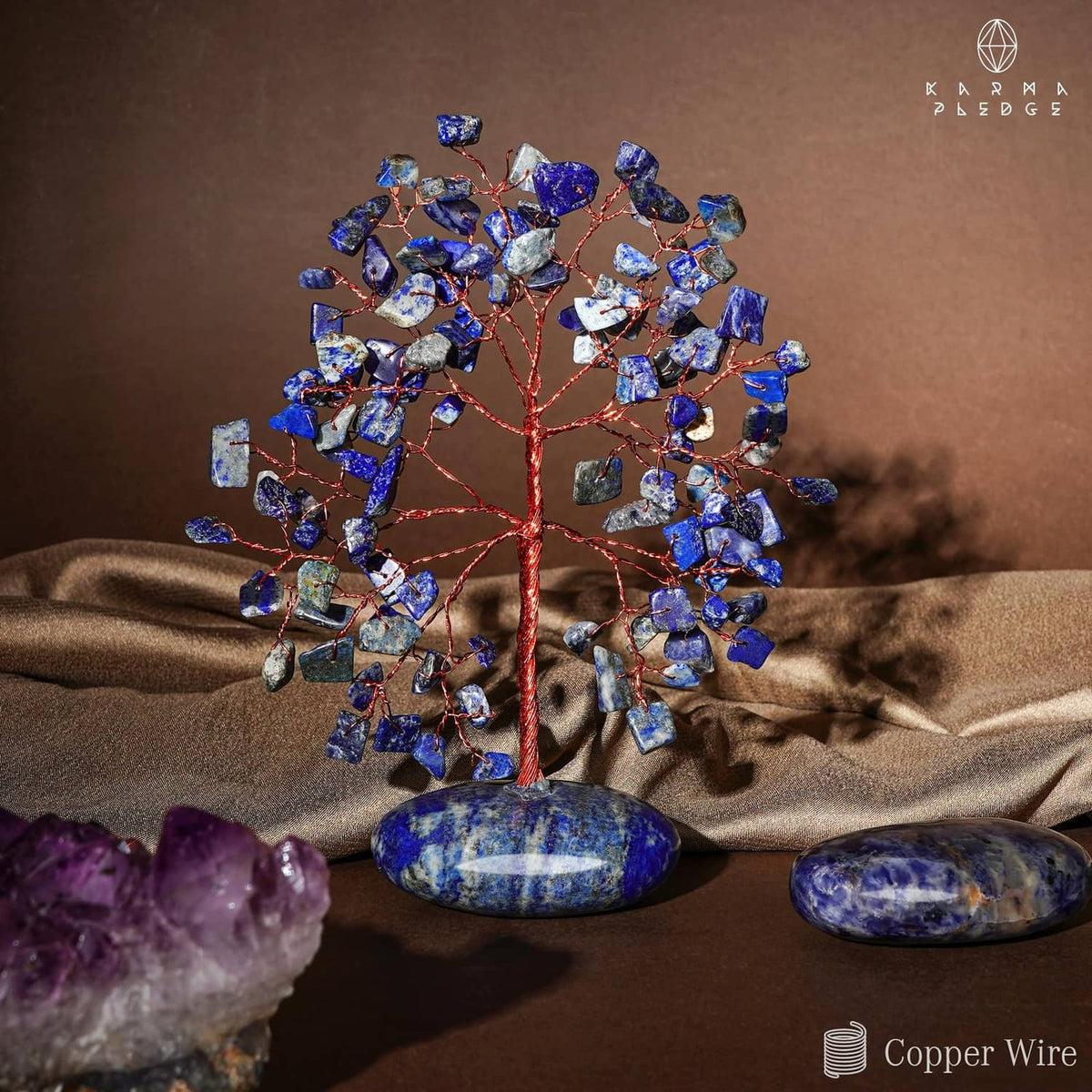 Blue lapis lazuli crystal tree with red wire and oval base stones on tabletop