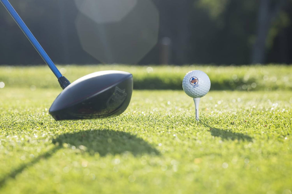 White wood golf tee with golf ball on grass beside a club