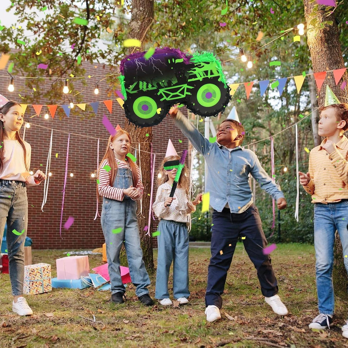 Monster truck piñata with green and purple design, held up at a kids' party