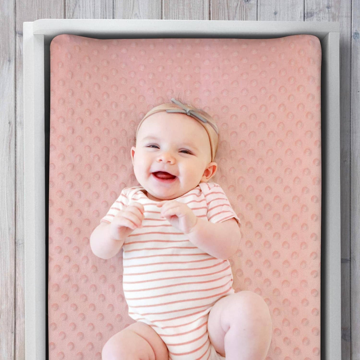 Peach-pink minky changing pad cover with dot texture and white flower and rainbow motifs