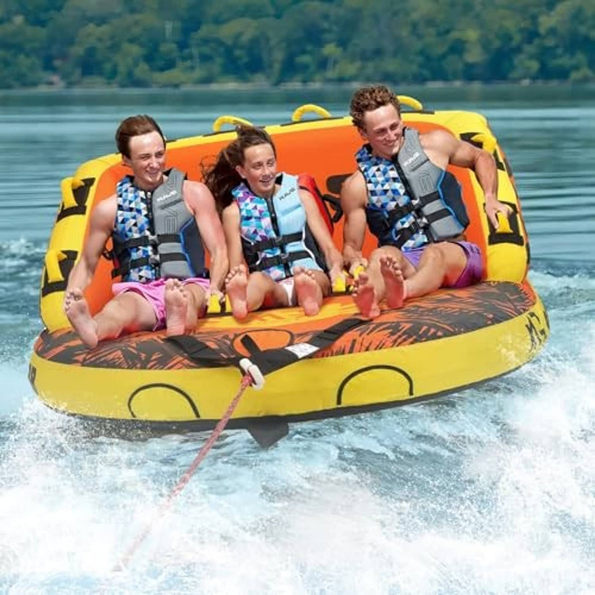 Inflatable orange and yellow towable tube carrying three riders, outdoor lake