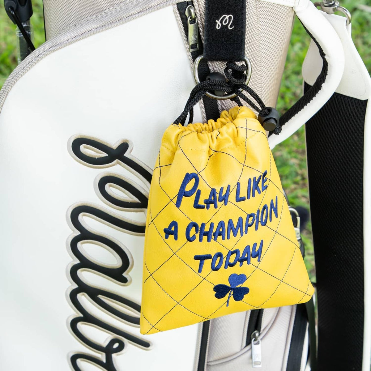 Yellow drawstring pouch hanging on a golf bag, featuring blue "Play Like a Champion Today" print.