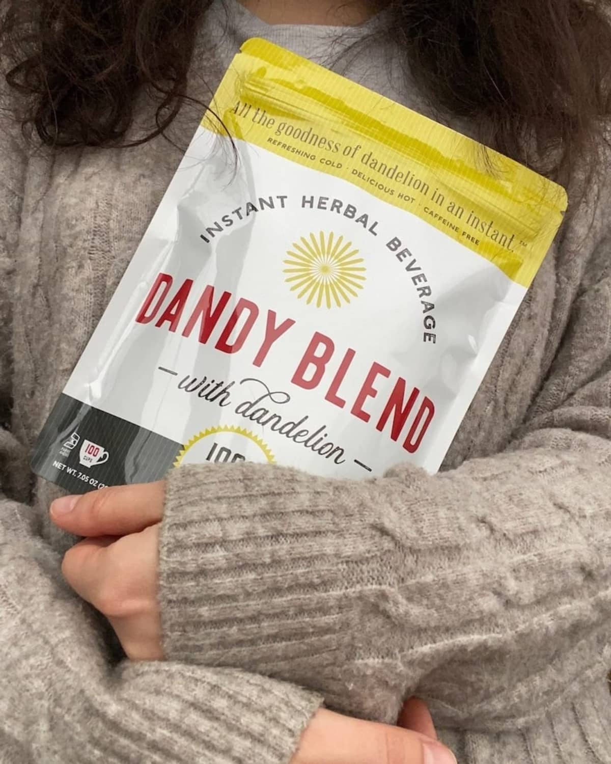 Instant herbal beverage pouch held by a person in a gray sweater