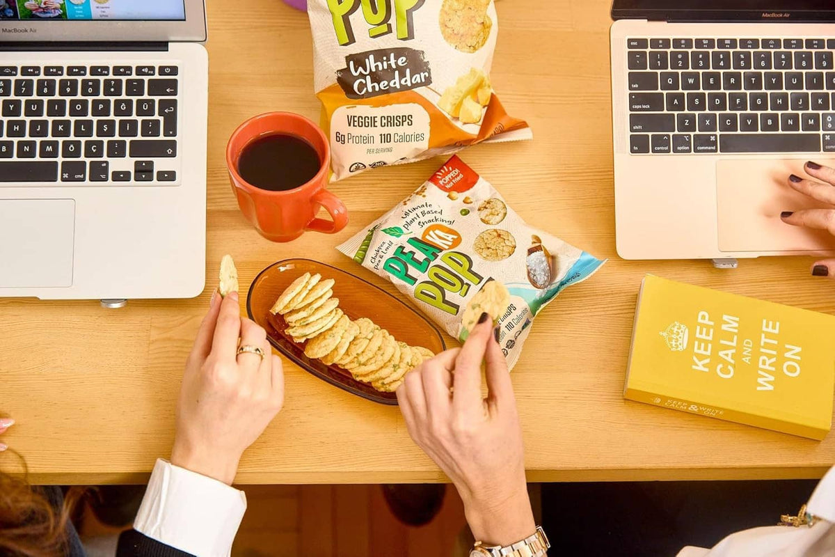 Hands holding Pea Ka Pop White Cheddar veggie crisps bag with a dip cup nearby