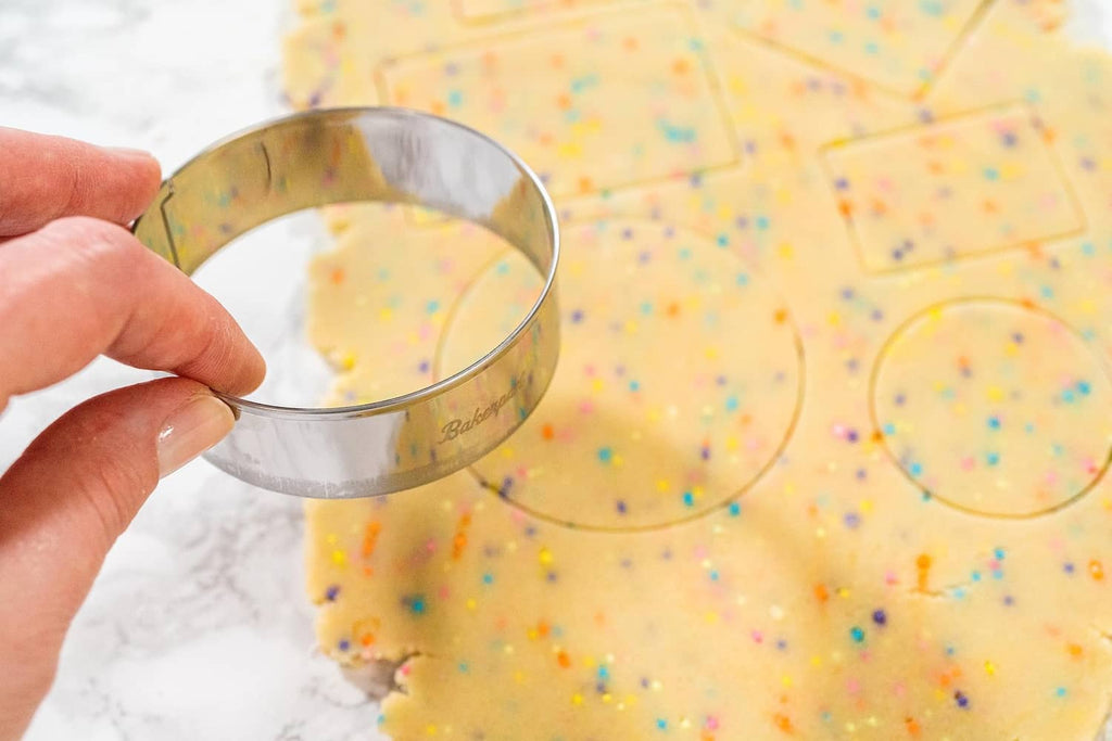 Hand holding a stainless steel round cookie cutter over sprinkle dough.