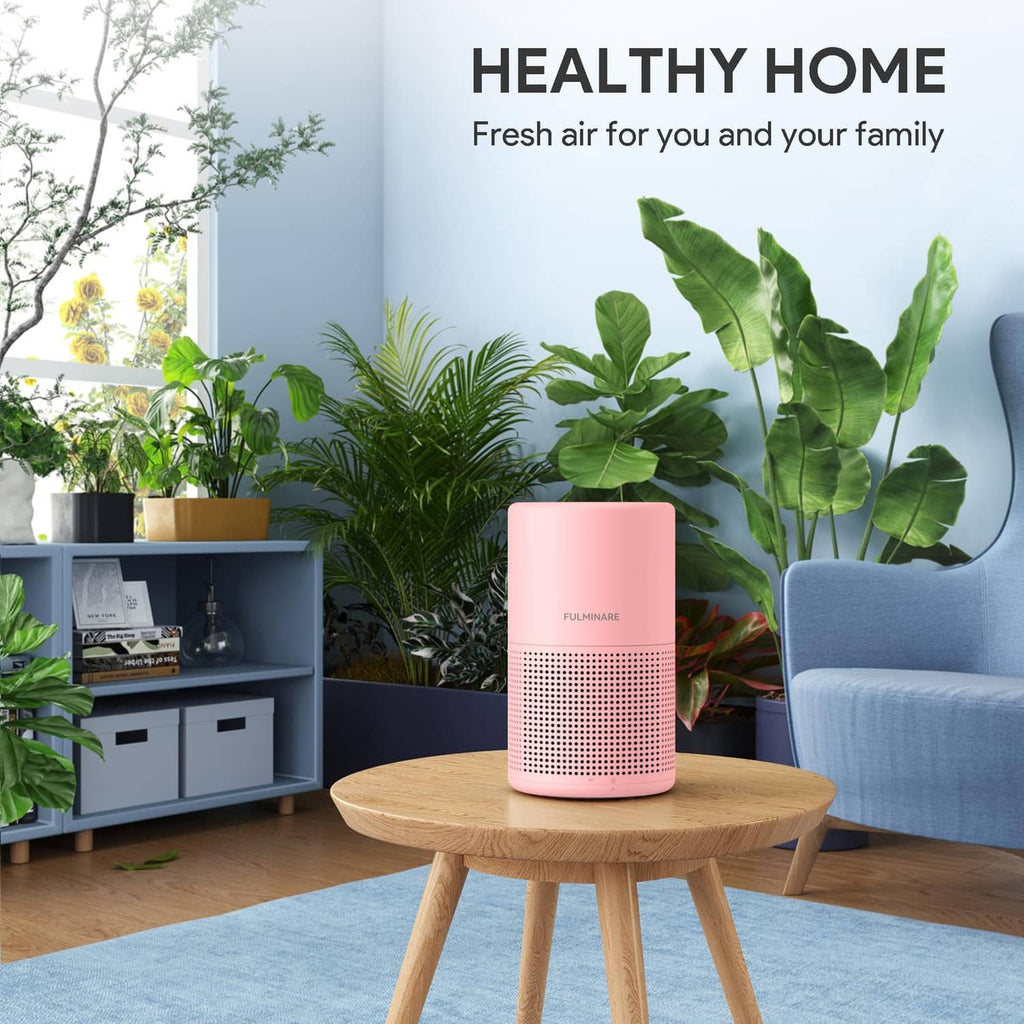 Pink air purifier cylinder with perforated grille on a round wooden coffee table