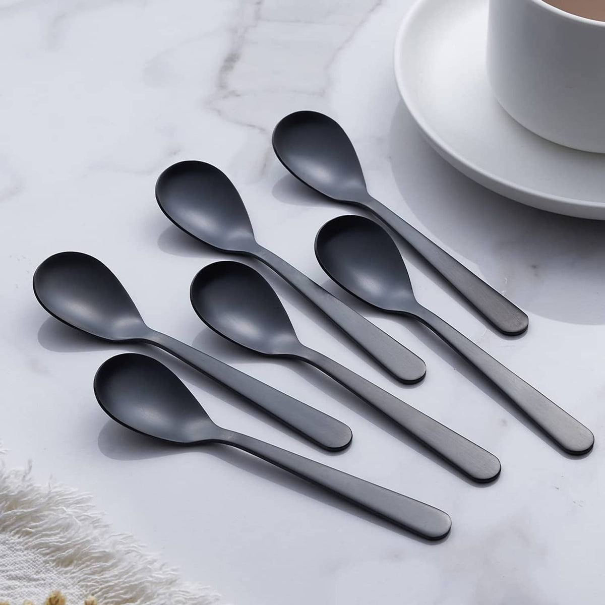 Matte black demitasse espresso spoons, rounded bowls on display with cup