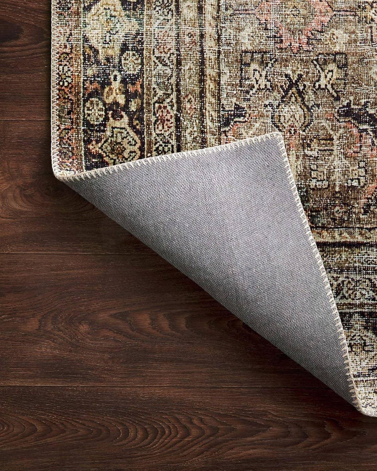 Area rug with textured backing visible at corner; muted olive, cream, and charcoal pattern