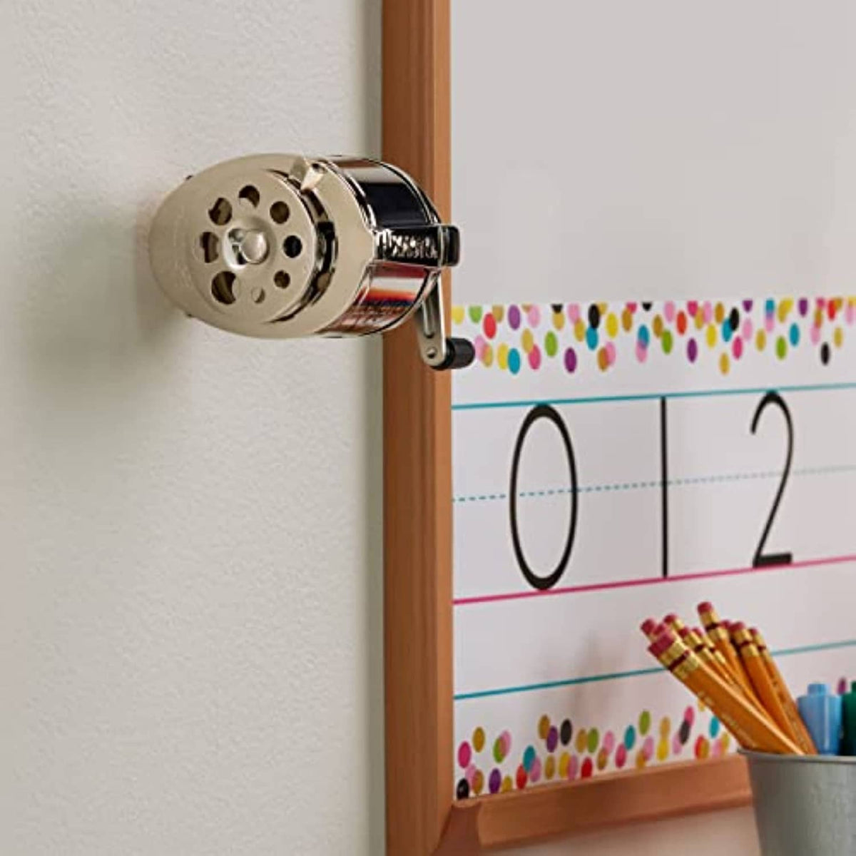 Chrome manual pencil sharpener on wall with black latch and visible crank knob