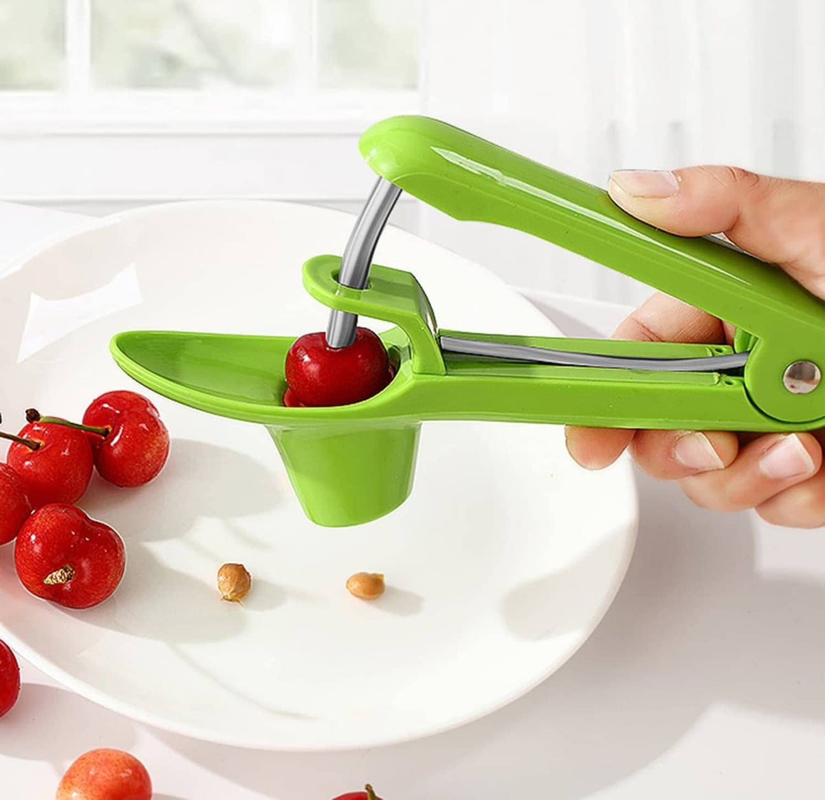 Green cherry pitter tool with metal prongs, holding a cherry over the catcher cup