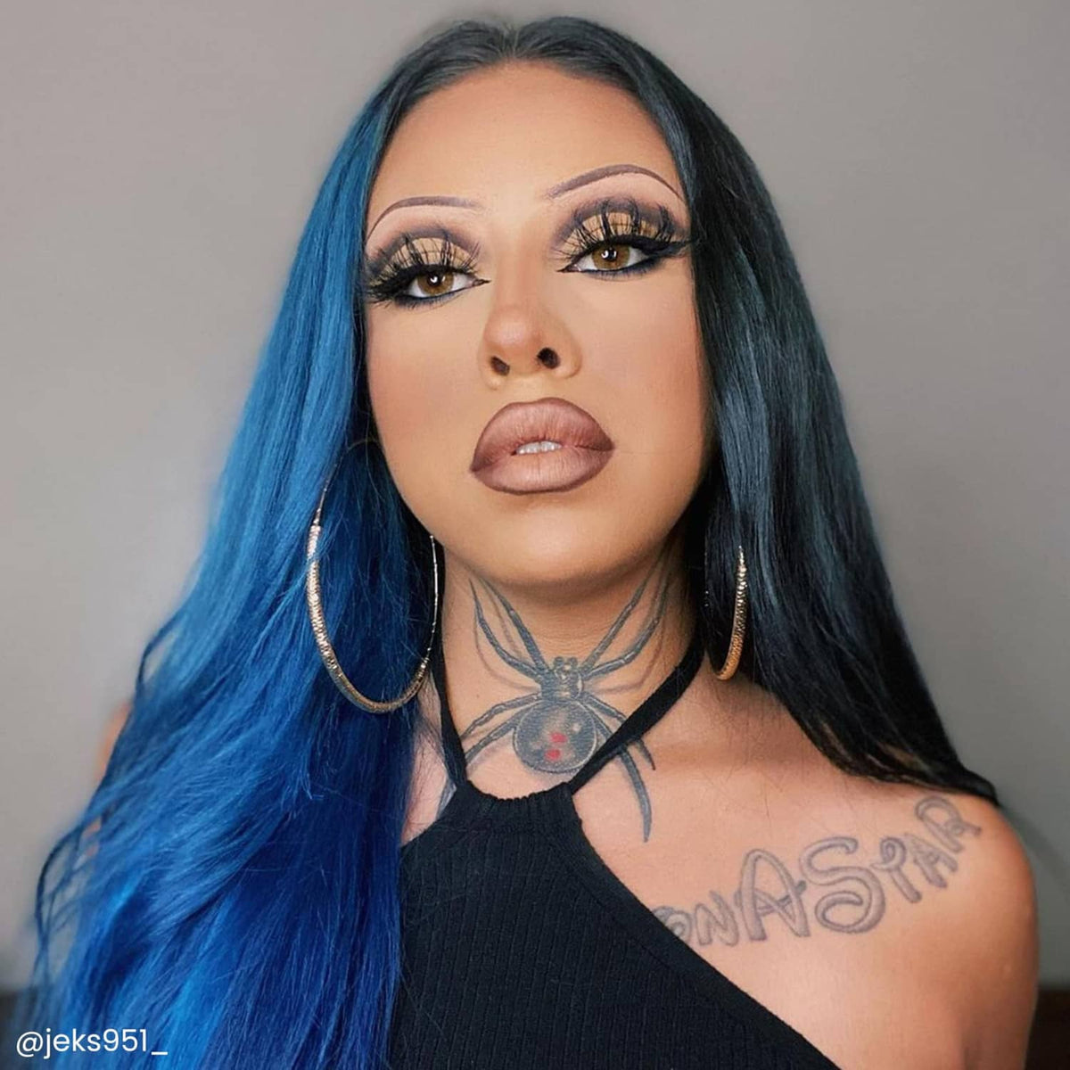 Blue-dyed hair section on long dark hair, styled with side bangs and makeup.