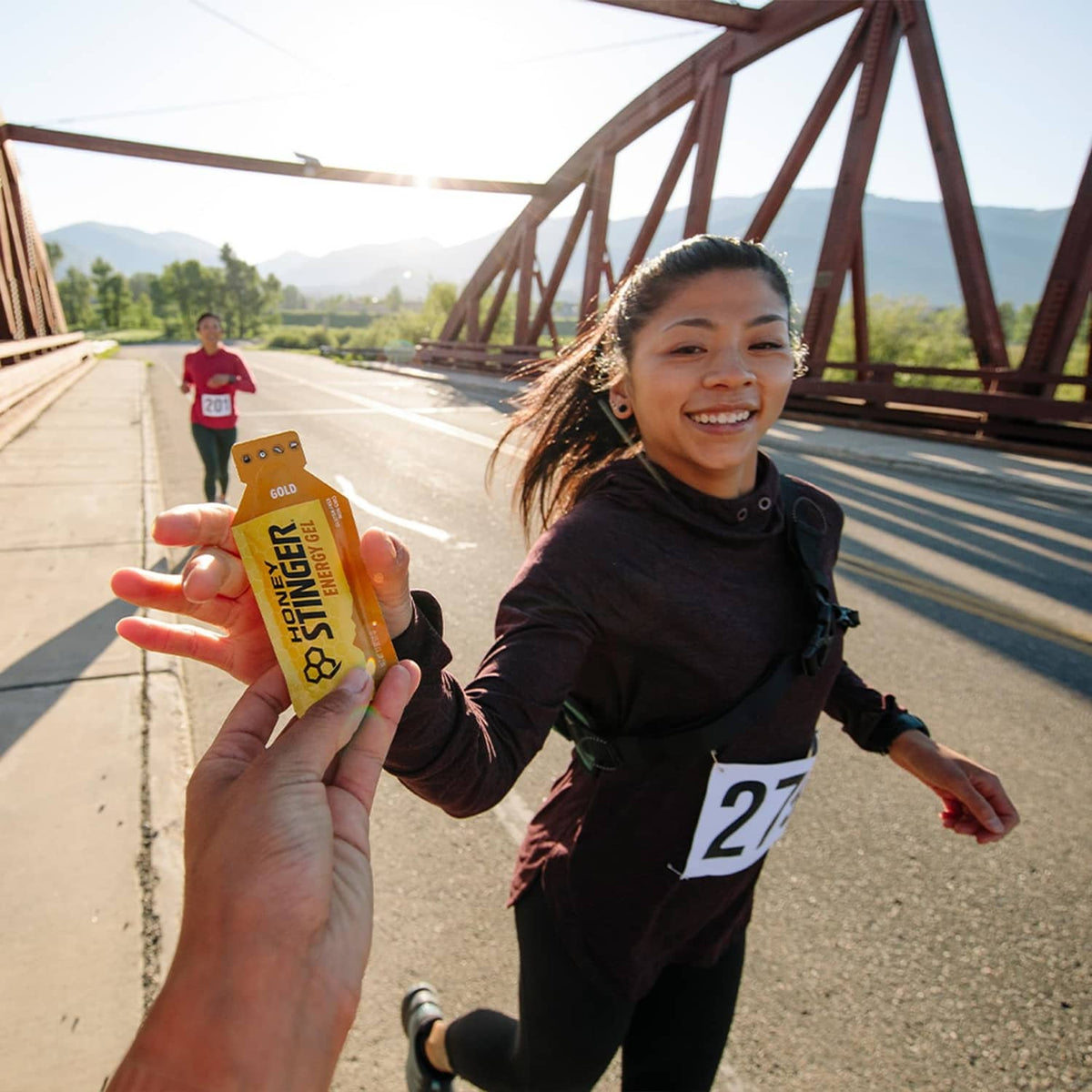 Runner holding a Honey Stinger Gold energy gel packet near a roadway race