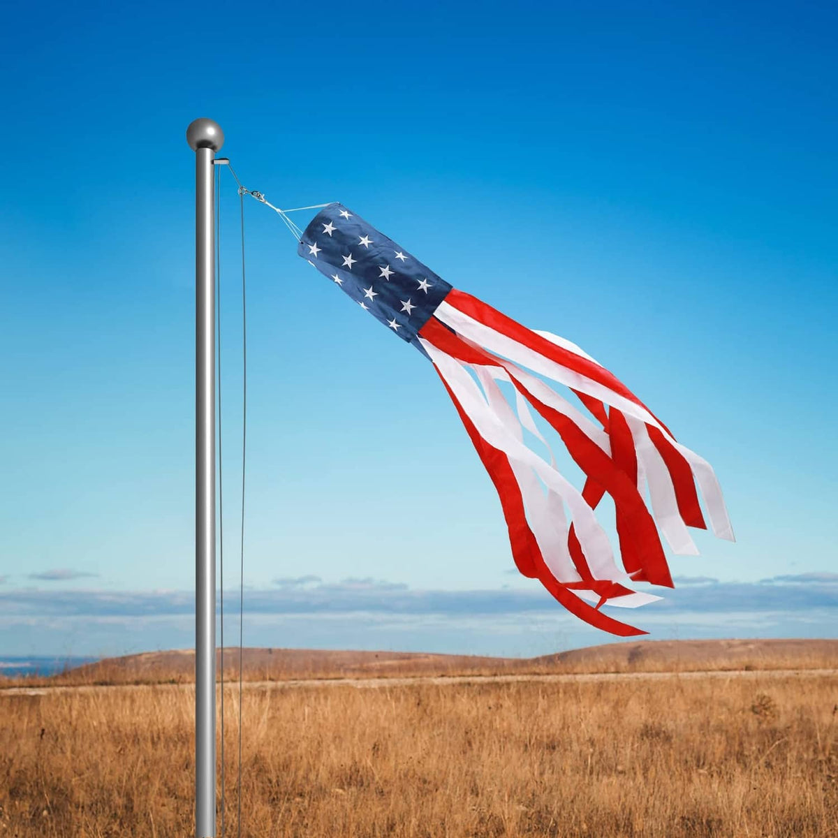 US flag windsock on a tall pole waving over an open field
