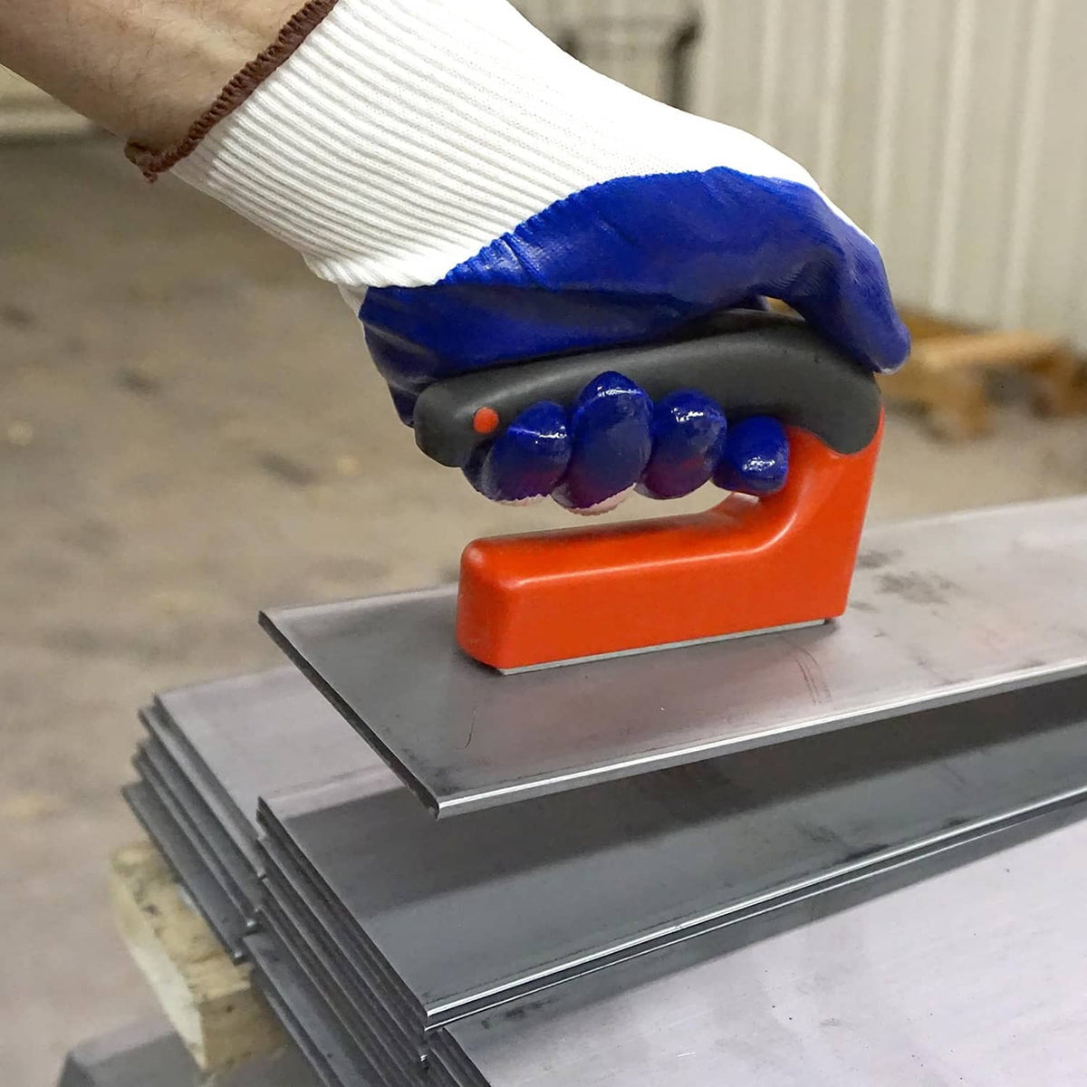 Orange handle magnet pressed onto metal rail with gloved blue hand