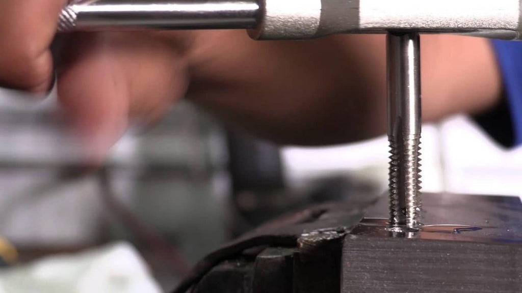 Close-up of tap cutting threads into a metal block