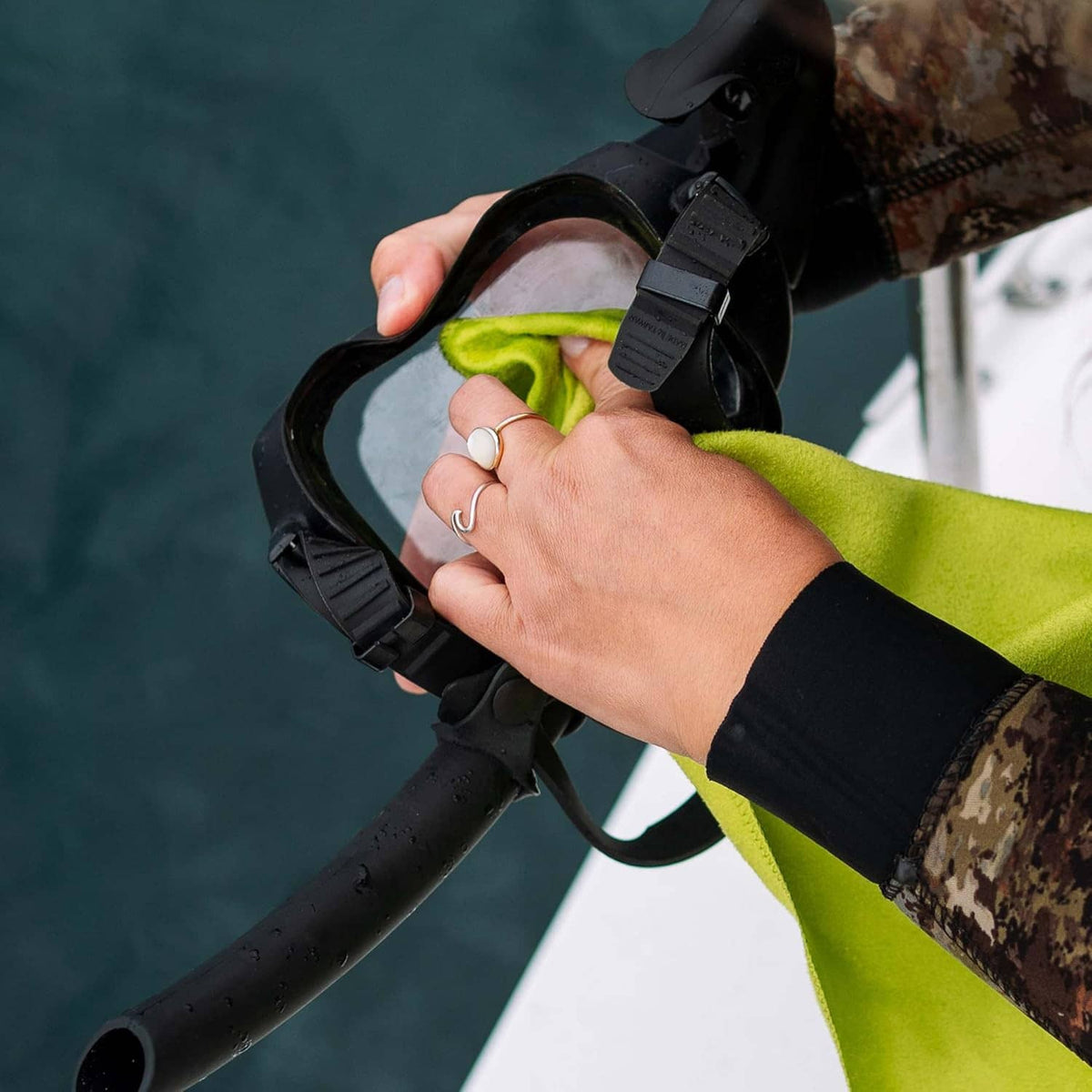 Anti-fog lens cleaner bottle drops being rubbed onto swim goggles