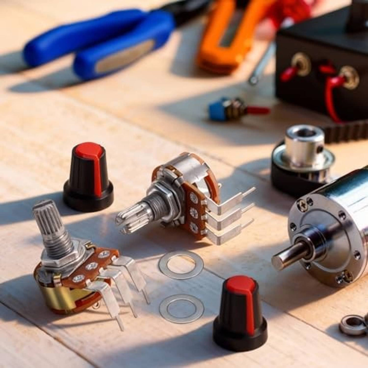 Rotary potentiometers set on a wooden workbench, black/red knobs and silver metal shafts