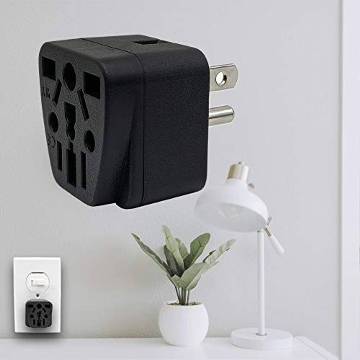 Black travel plug adapter mounted on wall with two metal prongs and socket holes