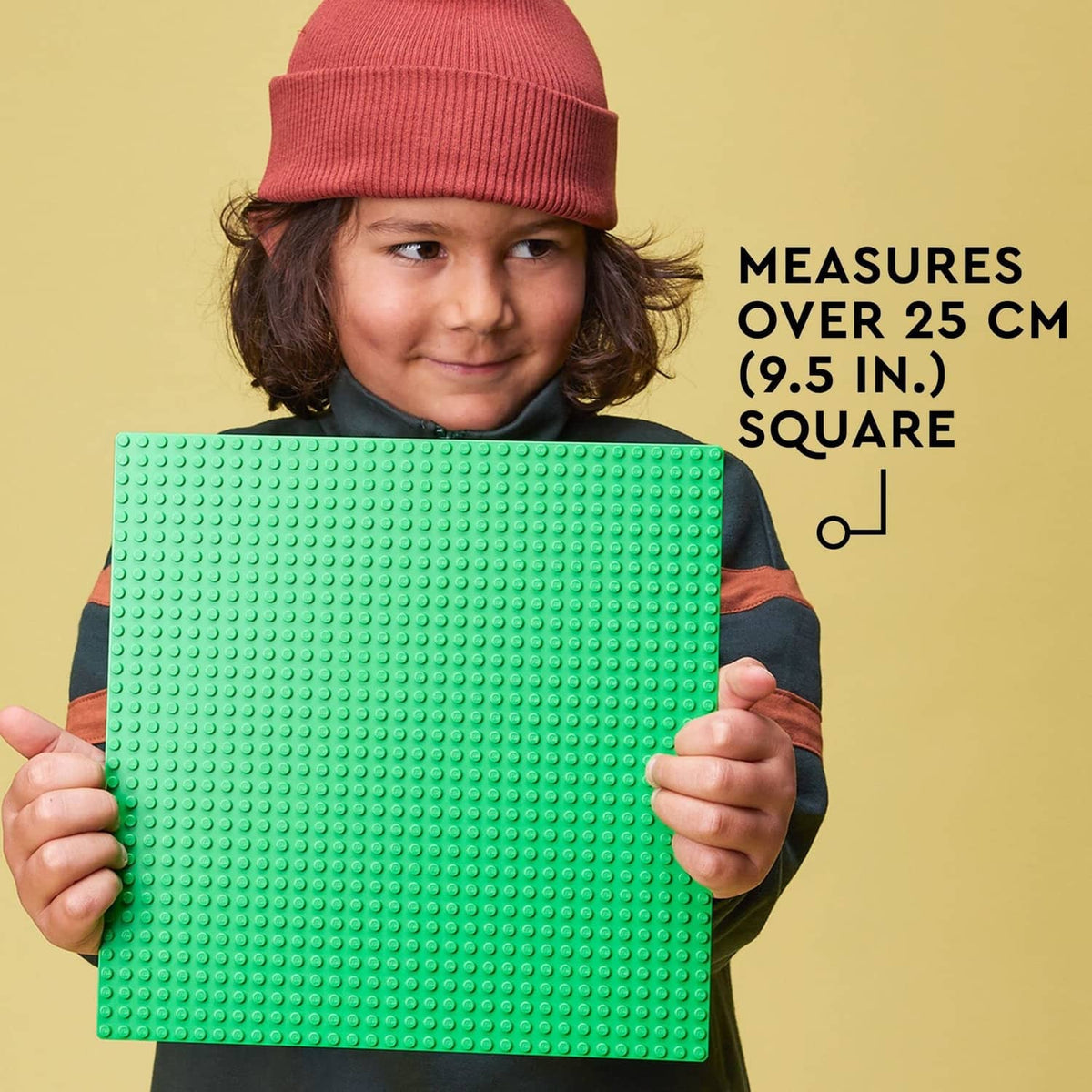 Green square LEGO baseplate, raised-stud surface, held up to show size.