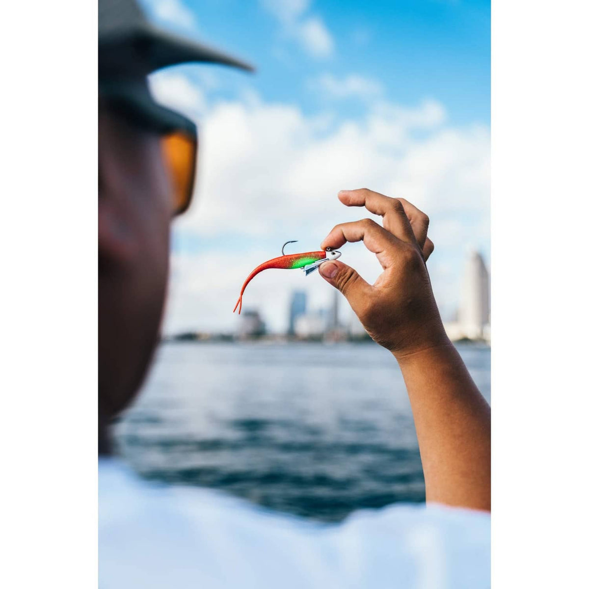 Hands holding red-green fishing lure with jig hook above the water