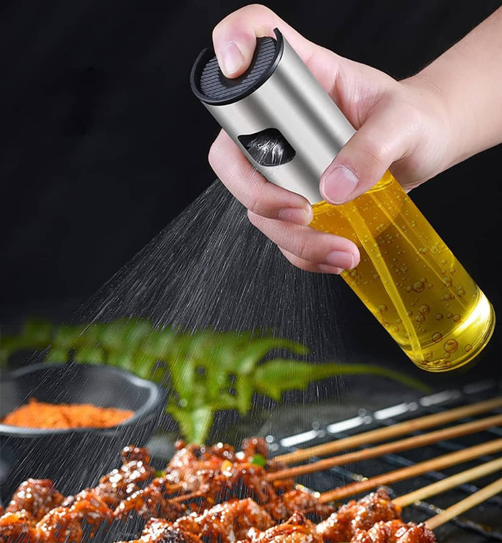 Stainless steel oil sprayer bottle with yellow liquid spraying fine mist over food