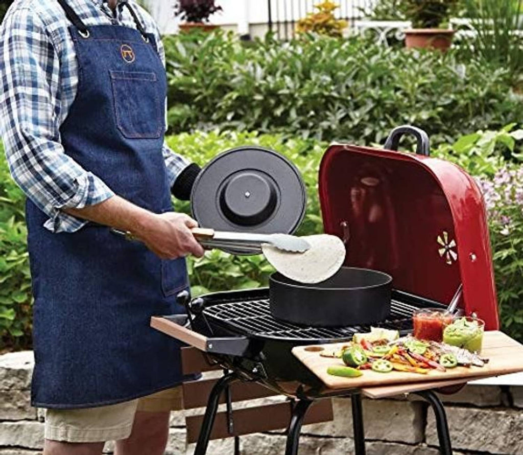 Blue denim apron with cross-back straps and two front pockets worn while grilling